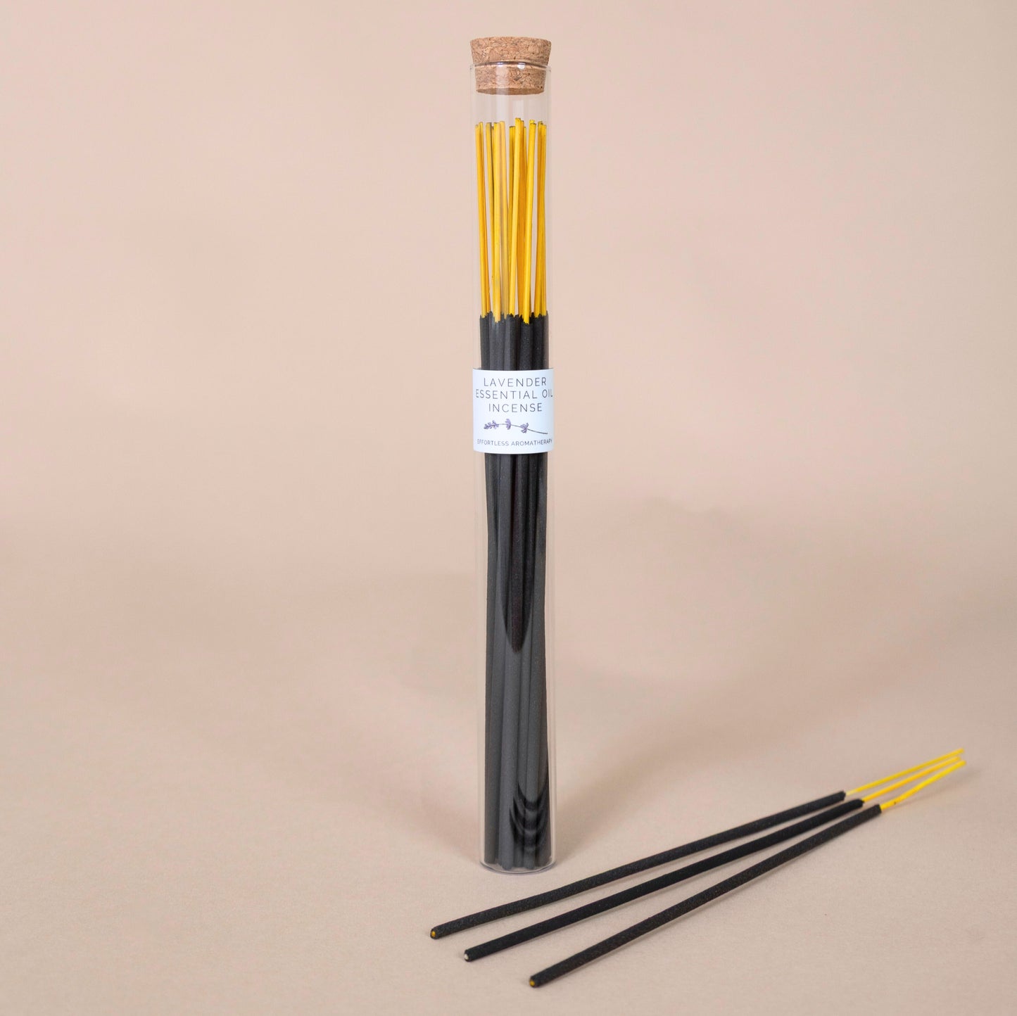 Tube of lavender incense sticks with three sticks displayed in front on a beige background