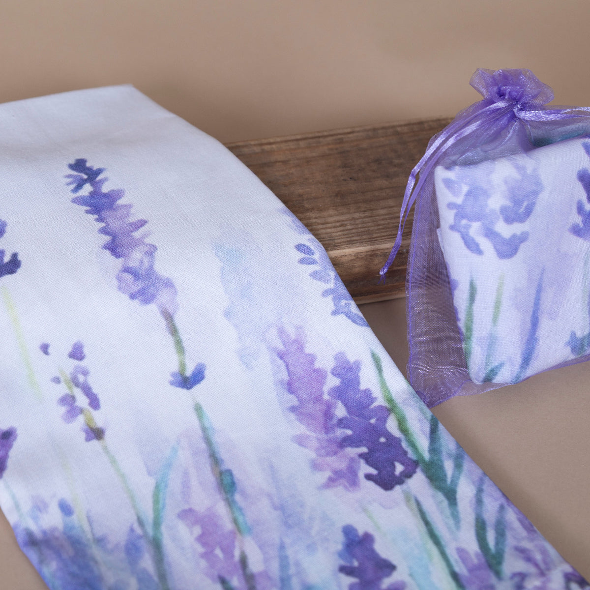 Lavender-themed kitchen towel displayed on a wooden surface and packaged in an small purple bag on a beige background