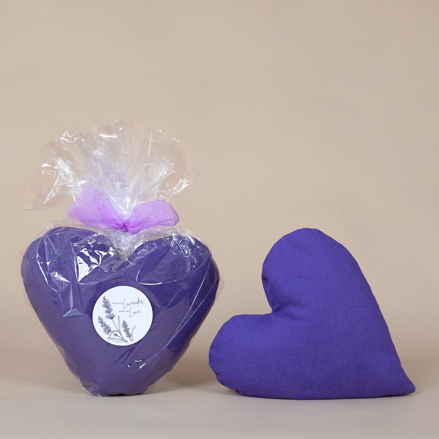 Lavender Heart Pillow displayed in purple, heart-shaped form, wrapped in cellophane with a bow on a beige background