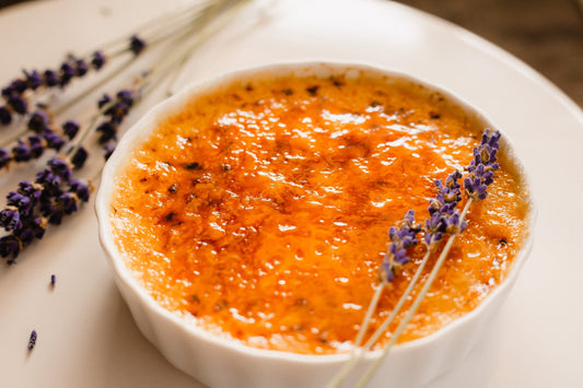 Lavender creme brulee in a white dish with lavender flowers on it on a white background.