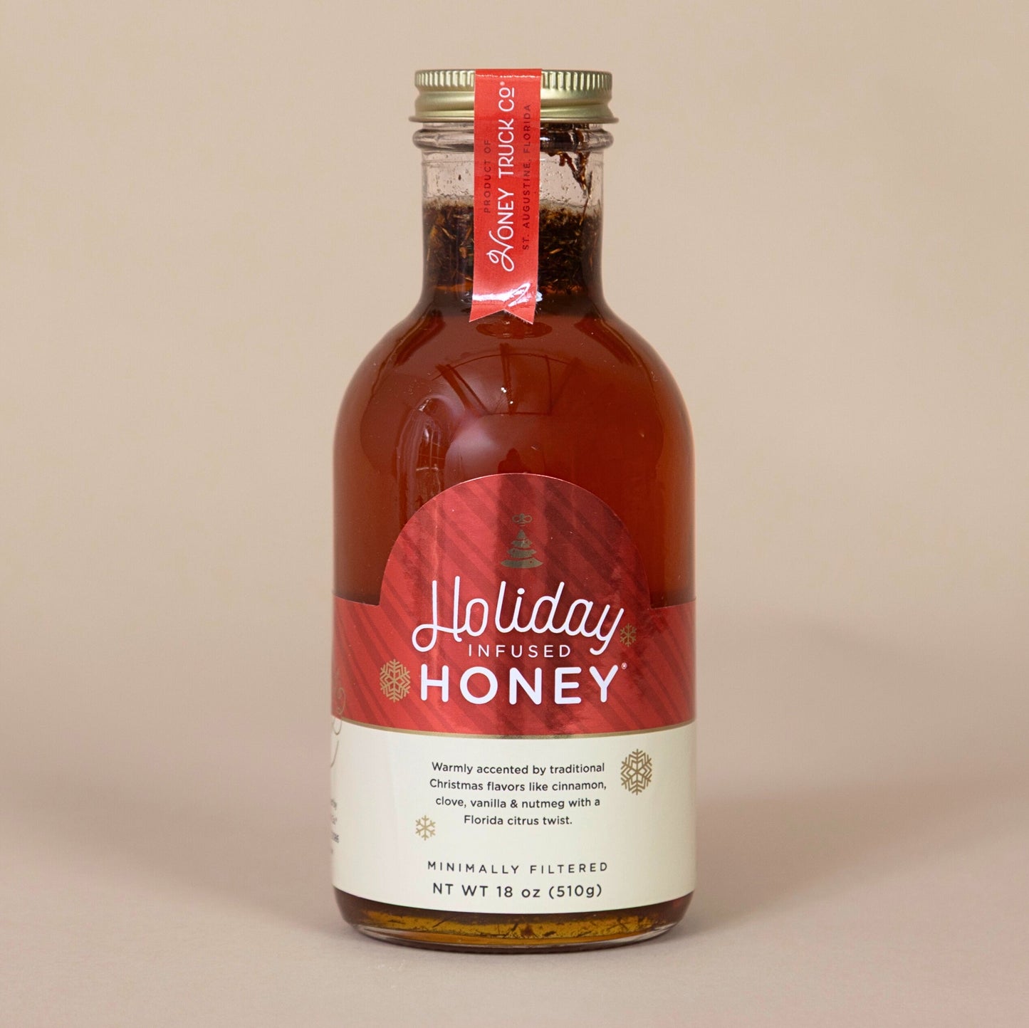 Holiday Honey bottle with a festive red label displayed on a beige background for a seasonal treat