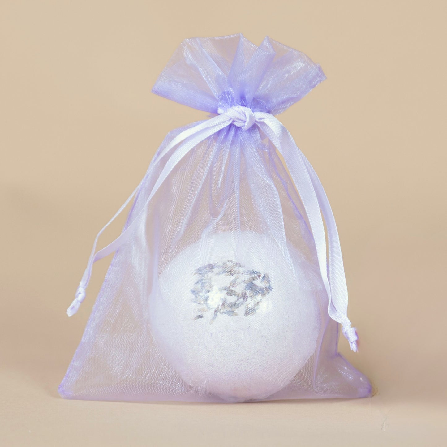 White bath bomb with lavender flowers in a purple drawstring bag on a beige background
