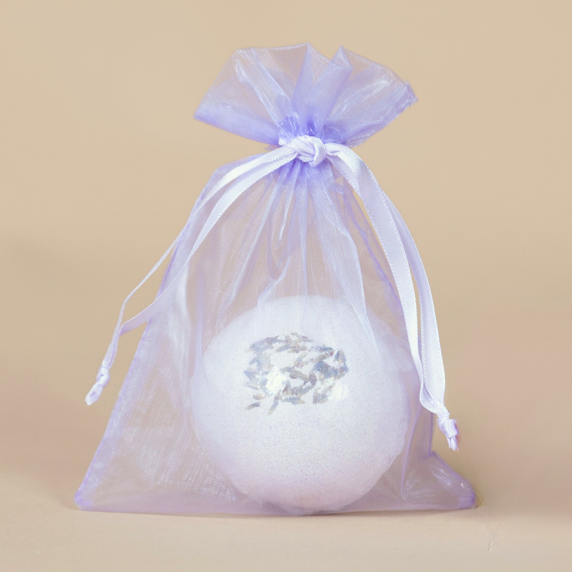 White bath bomb with lavender flowers in a purple drawstring bag on a beige background