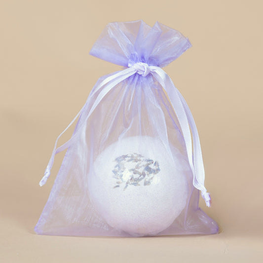 White bath bomb with lavender flowers in a purple drawstring bag on a beige background