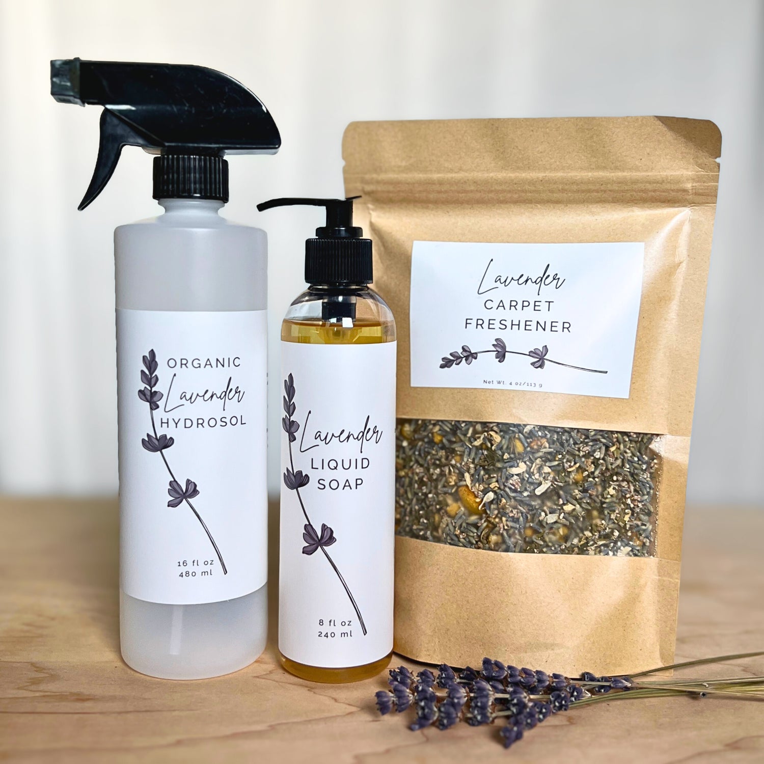 Bottle of lavender hydrosol, lavender soap and kraft back of lavender carpet freshener with lavender flowers on a white and wooden background