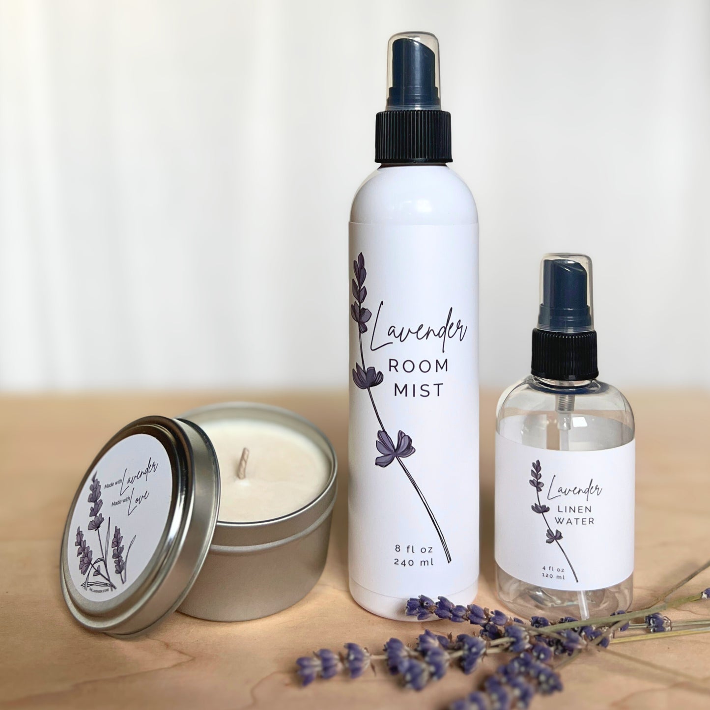 Lavender candle, bottle of lavender linen water and bottle of room mist with lavender flowers on a wood and white background