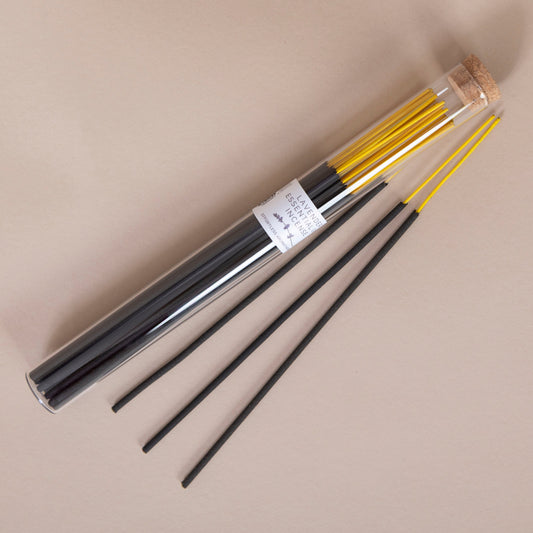 Set of black and yellow lavender incense sticks in a cylindrical packaging on a beige background