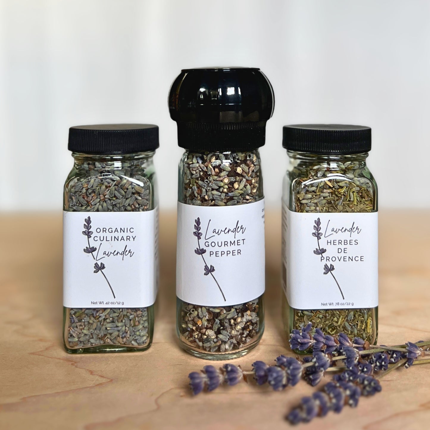 Glass jars of organic culinary lavender, lavender pepper and lavender herbes de provence with lavender flowers on a wood and white background