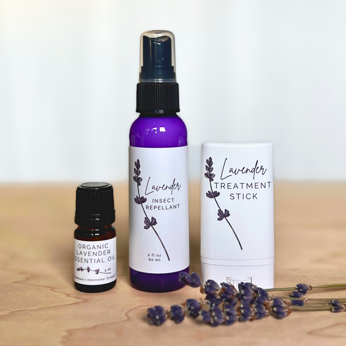 Lavender Insect Repellant, bottle of organic lavender essential oil and white tube of lavender treatment stick with lavender flowers on a wood and white background