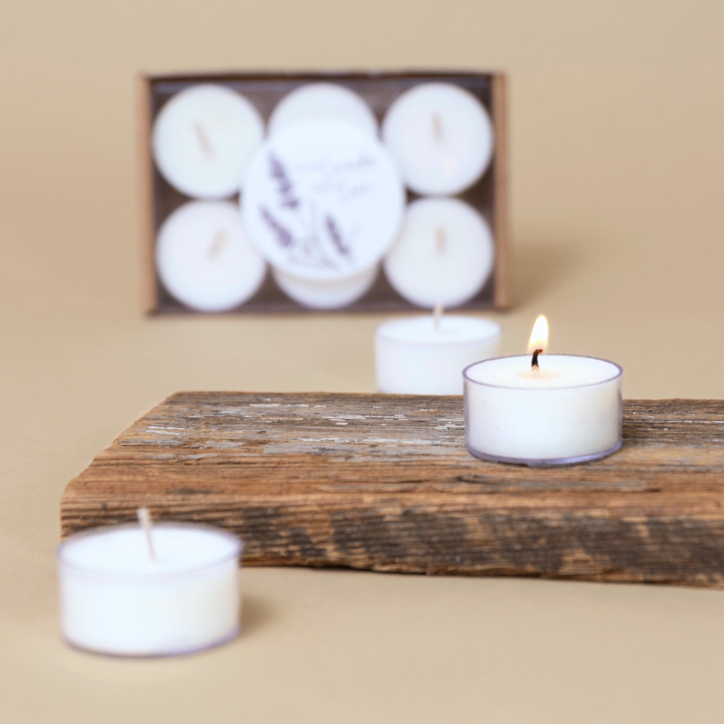 White lavender tealight candles on wood tray and boxed on a beige background